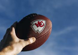 Hand holding a football with the logo for the Kansas City Chiefs on it
